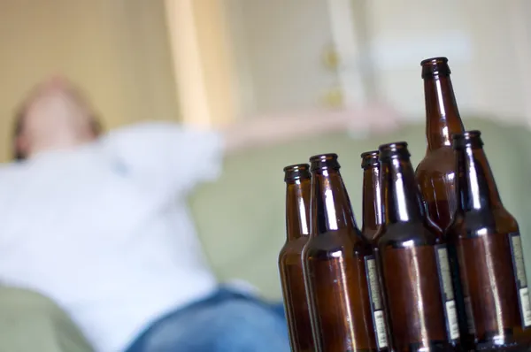 El hombre se desmayó en el sofá con botellas de cerveza vacías, en ángulo Imagen de archivo