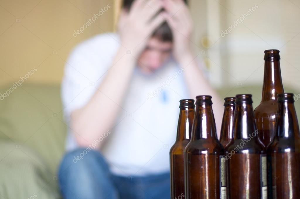 Man holds head with group of empty beer bottles