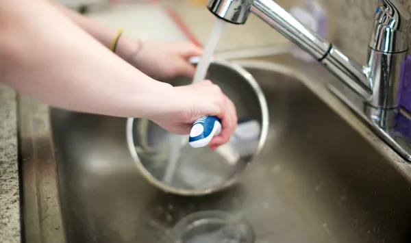 女性は、台所の流しの金属製のボウルを洗う ロイヤリティフリーのストック画像