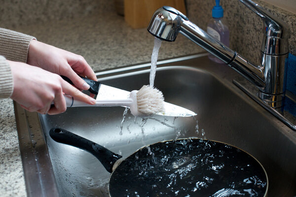 Close up of hands scrubbing knife in sink