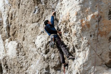 Genç adam arka planında geniş bir vadiyle kireçtaşı bir duvara tırmanıyor.