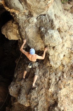 Genç adam arka planında geniş bir vadiyle kireçtaşı bir duvara tırmanıyor.