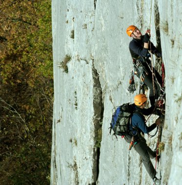 Genç adam arka planında geniş bir vadiyle kireçtaşı bir duvara tırmanıyor.