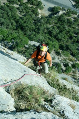 Genç adam arka planında geniş bir vadiyle kireçtaşı bir duvara tırmanıyor.