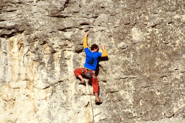 Hombre joven escalando pared vertical con vista al valle en el fondo —  Fotos de Stock