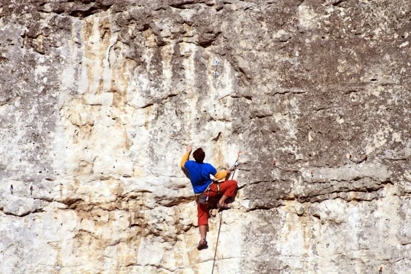 Hombre joven escalando pared vertical con vista al valle en el fondo — Foto de Stock