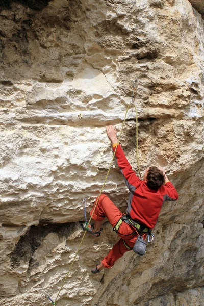 Young man climbing vertical wall with valley view on the background — Stock Photo, Image