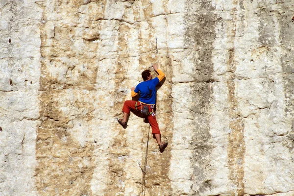 Hombre joven escalando pared vertical con vista al valle en el fondo — Foto de Stock