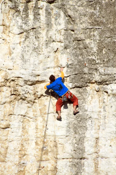 Hombre joven escalando pared vertical con vista al valle en el fondo —  Fotos de Stock