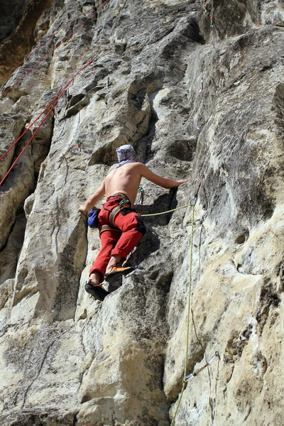 Young man climbing vertical wall with valley view on the background — Stock Photo, Image