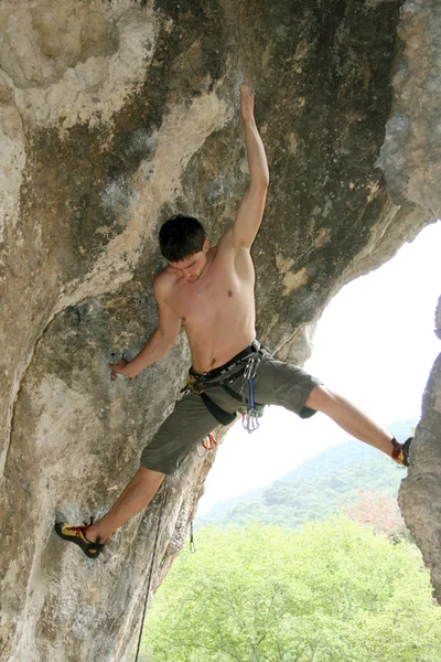 Junger Mann klettert senkrechte Wand mit Talblick im Hintergrund — Stockfoto