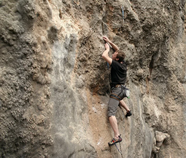 Young man climbing vertical wall with valley view on the background — Stock Photo, Image