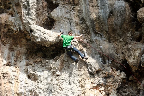 Young man climbing vertical wall with valley view on the background — Stock Photo, Image