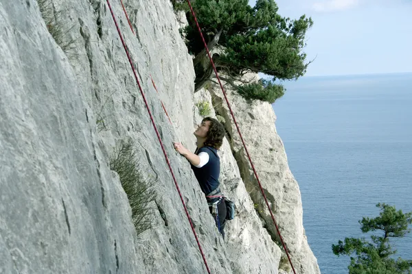 Junger Mann klettert senkrechte Wand mit Talblick im Hintergrund — Stockfoto