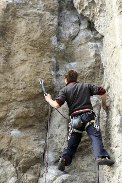 Hombre joven escalando pared vertical con vista al valle en el fondo — Foto de Stock