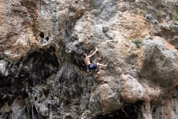Junger Mann klettert senkrechte Wand mit Talblick im Hintergrund — Stockfoto
