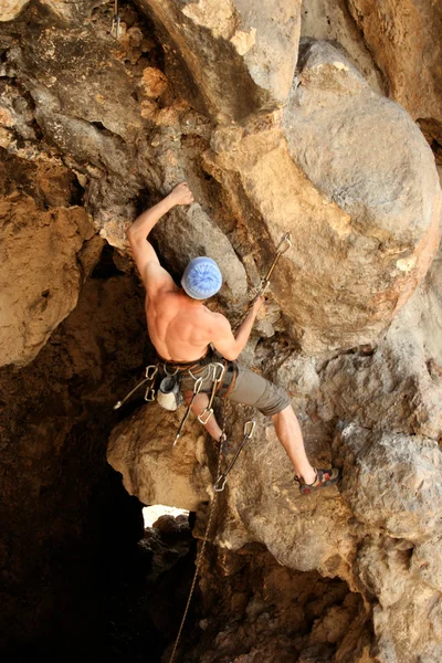 Hombre joven escalando pared vertical con vista al valle en el fondo — Foto de Stock