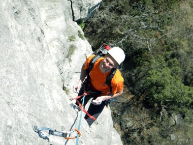 Genç adam arka planında geniş bir vadiyle kireçtaşı bir duvara tırmanıyor.