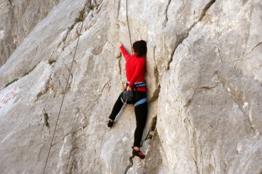 Genç adam arka planında geniş bir vadiyle kireçtaşı bir duvara tırmanıyor.
