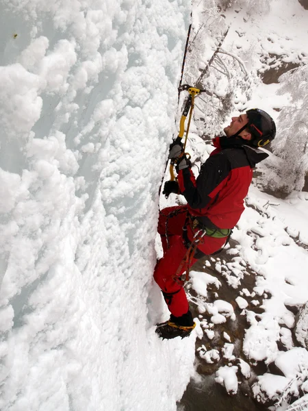 Escalador de hielo lucha por una cascada congelada . — Foto de Stock