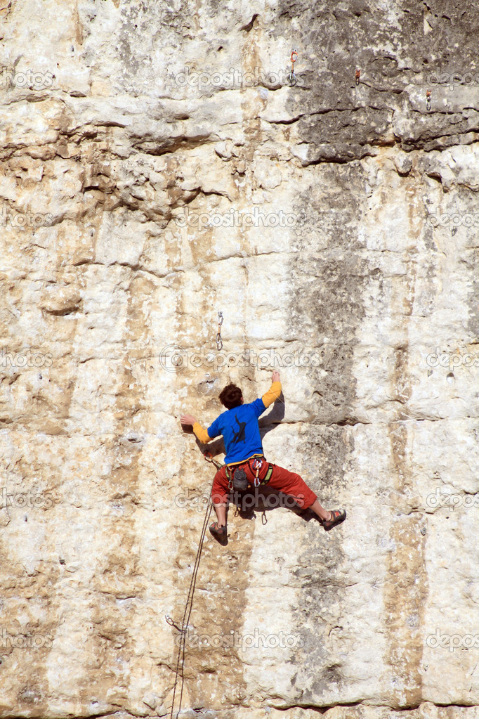 Young man climbing on a limestone wall with wide valley on the background