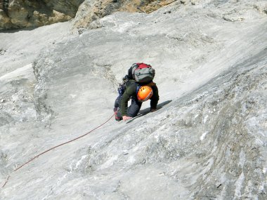 Genç adam arka planında geniş bir vadiyle kireçtaşı bir duvara tırmanıyor.