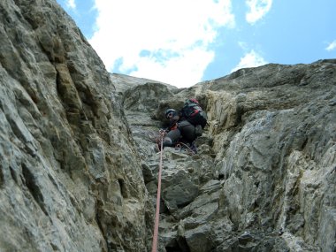 Genç adam arka planında geniş bir vadiyle kireçtaşı bir duvara tırmanıyor.