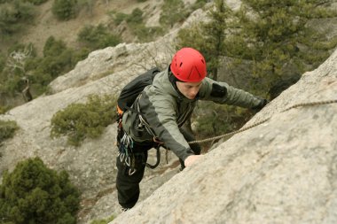 Genç adam arka planında geniş bir vadiyle kireçtaşı bir duvara tırmanıyor.