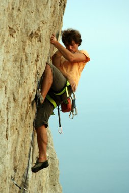 Genç adam arka planında geniş bir vadiyle kireçtaşı bir duvara tırmanıyor.