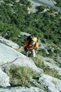 Genç adam arka planında geniş bir vadiyle kireçtaşı bir duvara tırmanıyor.