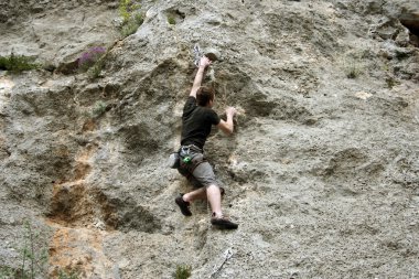 Genç adam arka planında geniş bir vadiyle kireçtaşı bir duvara tırmanıyor.