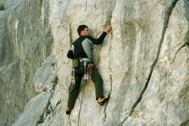 Genç adam arka planında geniş bir vadiyle kireçtaşı bir duvara tırmanıyor.