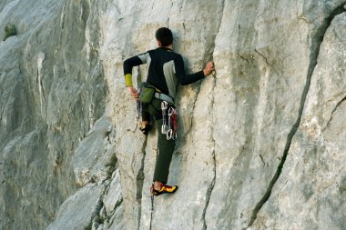 Genç adam arka planında geniş bir vadiyle kireçtaşı bir duvara tırmanıyor.