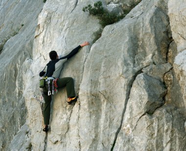 Genç adam arka planında geniş bir vadiyle kireçtaşı bir duvara tırmanıyor.