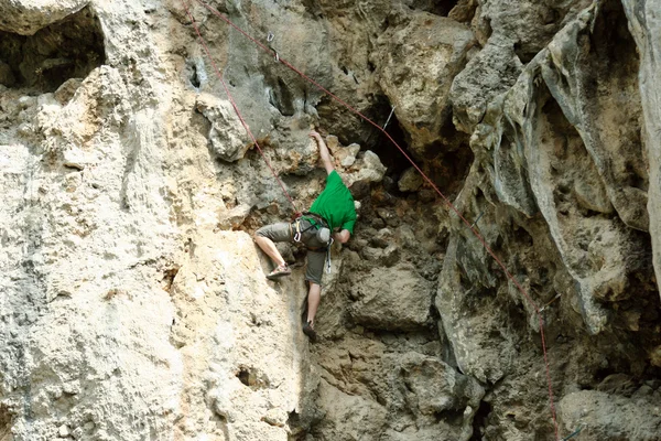 Hombre joven escalando pared vertical con vista al valle en el fondo —  Fotos de Stock