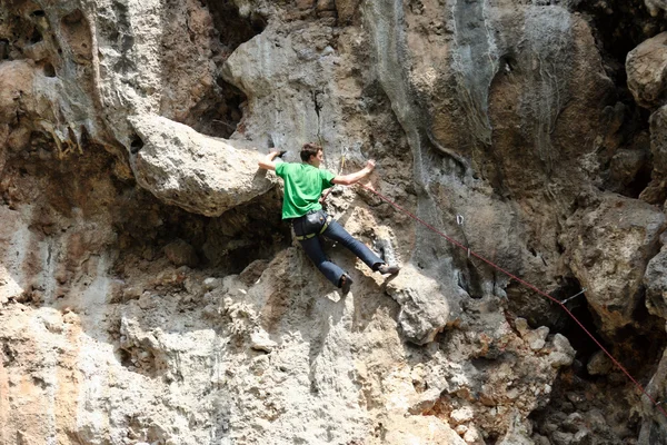 Young man climbing vertical wall with valley view on the background — Stock Photo, Image