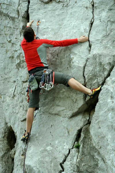 Jovem escalando parede vertical com vista para o vale no fundo — Fotografia de Stock