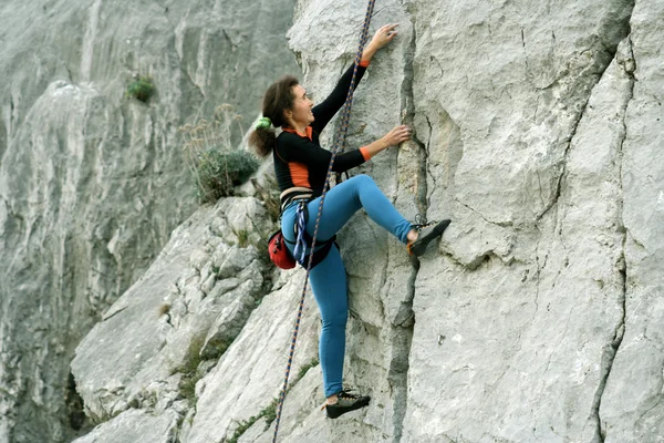 Mujer joven escalando pared vertical con vista al valle en el fondo —  Fotos de Stock