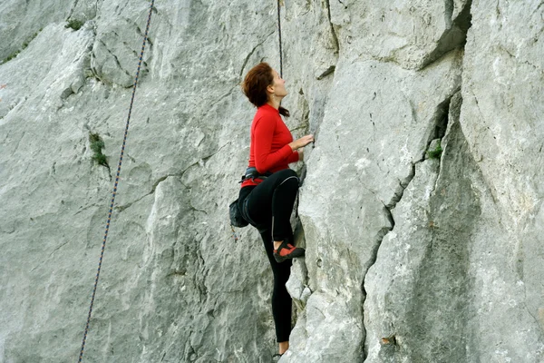 Junge Frau klettert senkrechte Wand mit Talblick im Hintergrund — Stockfoto