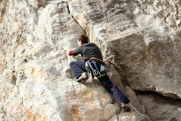 Young man climbing vertical wall with valley view on the background — Stock Photo, Image