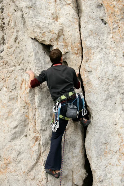 Junger Mann klettert senkrechte Wand mit Talblick im Hintergrund — Stockfoto