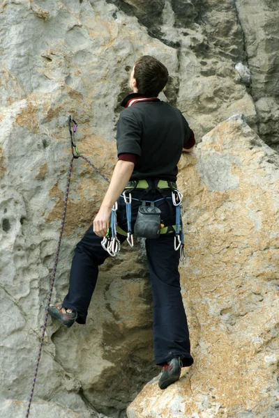 Young man climbing vertical wall with valley view on the background — Stock Photo, Image