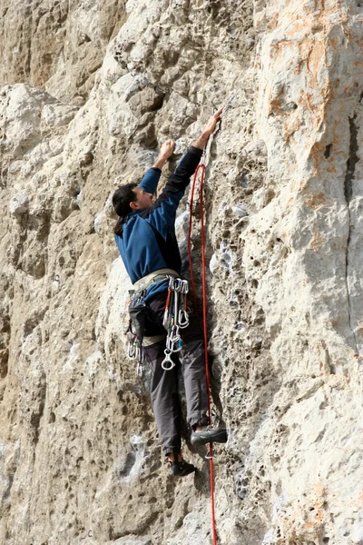 Hombre joven escalando pared vertical con vista al valle en el fondo — Foto de Stock