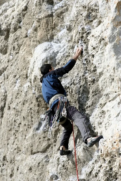 Hombre joven escalando pared vertical con vista al valle en el fondo — Foto de Stock