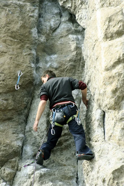 Hombre joven escalando pared vertical con vista al valle en el fondo —  Fotos de Stock