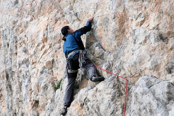 Young man climbing vertical wall with valley view on the background — Stock Photo, Image