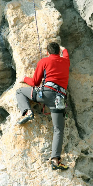 Young man climbing vertical wall with valley view on the background — Stock Photo, Image