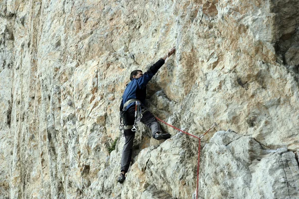 Young man climbing vertical wall with valley view on the background — Stock Photo, Image