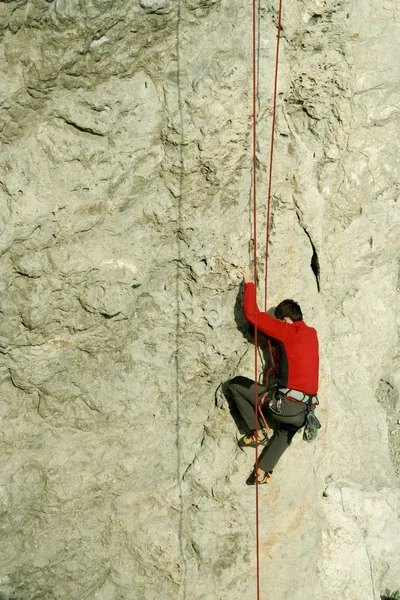 Young man climbing vertical wall with valley view on the background — Stock Photo, Image