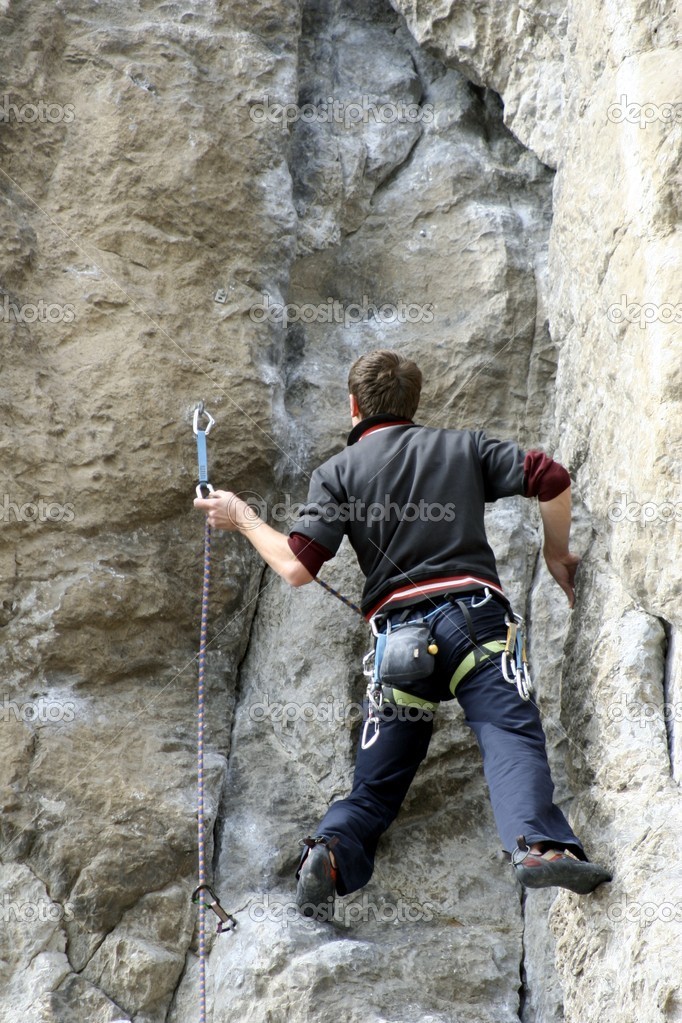 Young man climbing vertical wall with valley view on the background